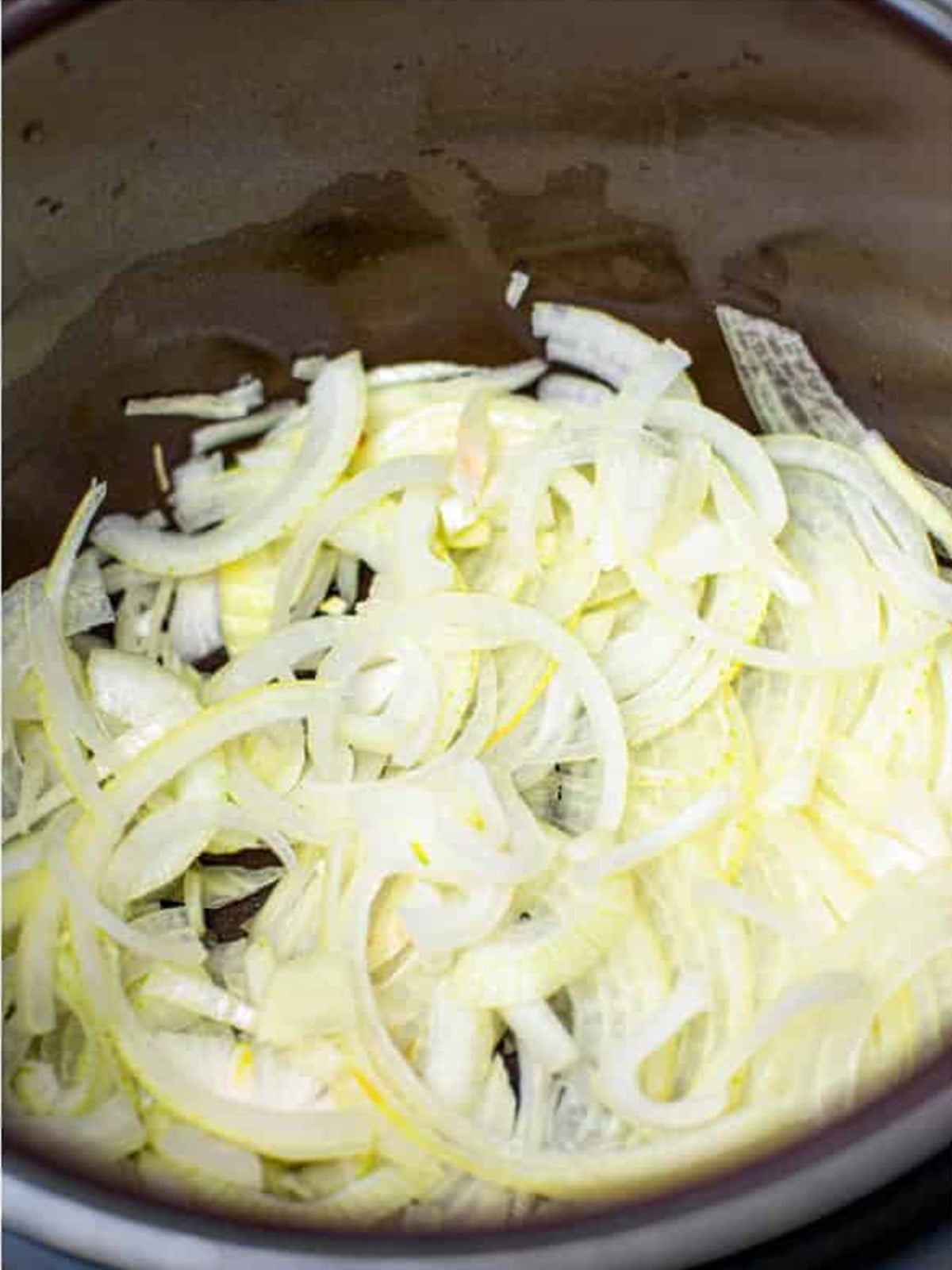 Sliced sweet onions layered in the bottom of a slow cooker for crock pot pulled pork.