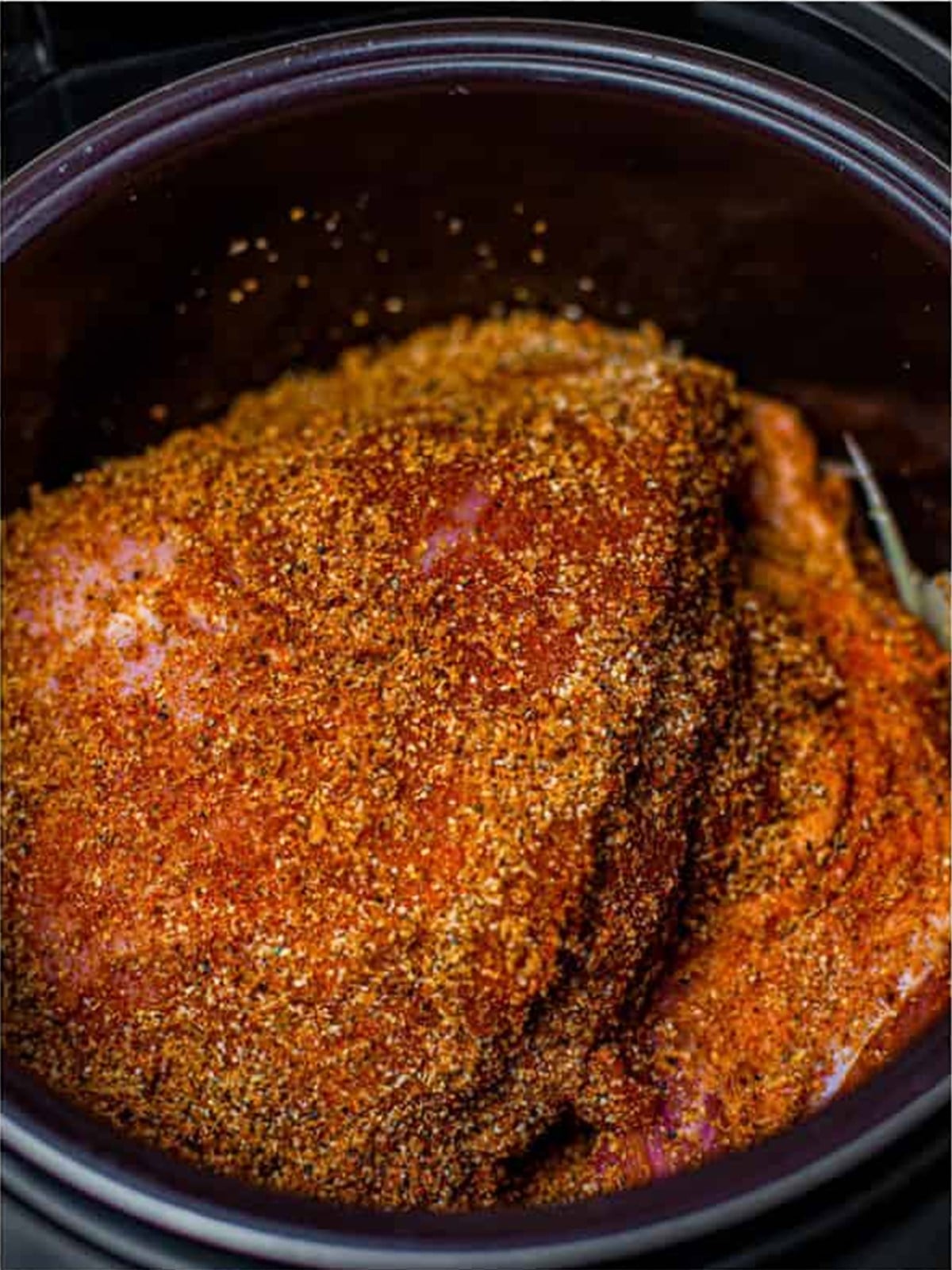 Pork shoulder rubbed with brown sugar and spice seasoning on top of the onions.