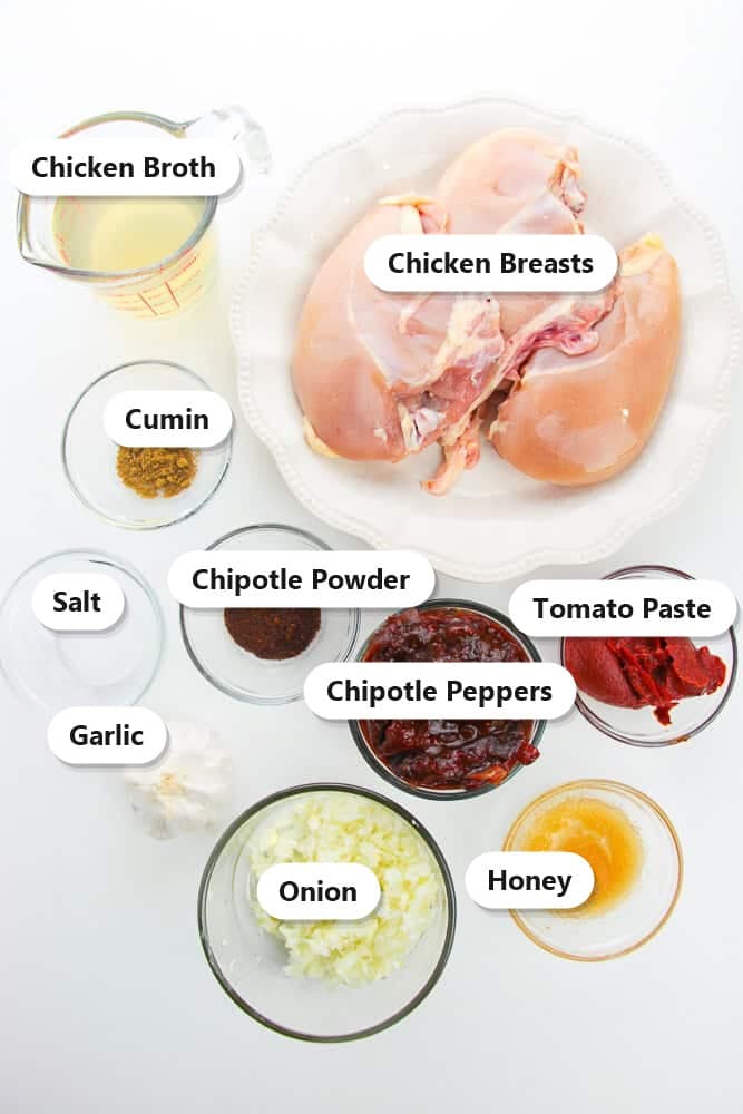 Labeled ingredients for crockpot chicken tacos including chicken breasts, chipotle peppers, tomato paste, honey, chicken broth, onion, garlic, cumin, and chipotle powder.