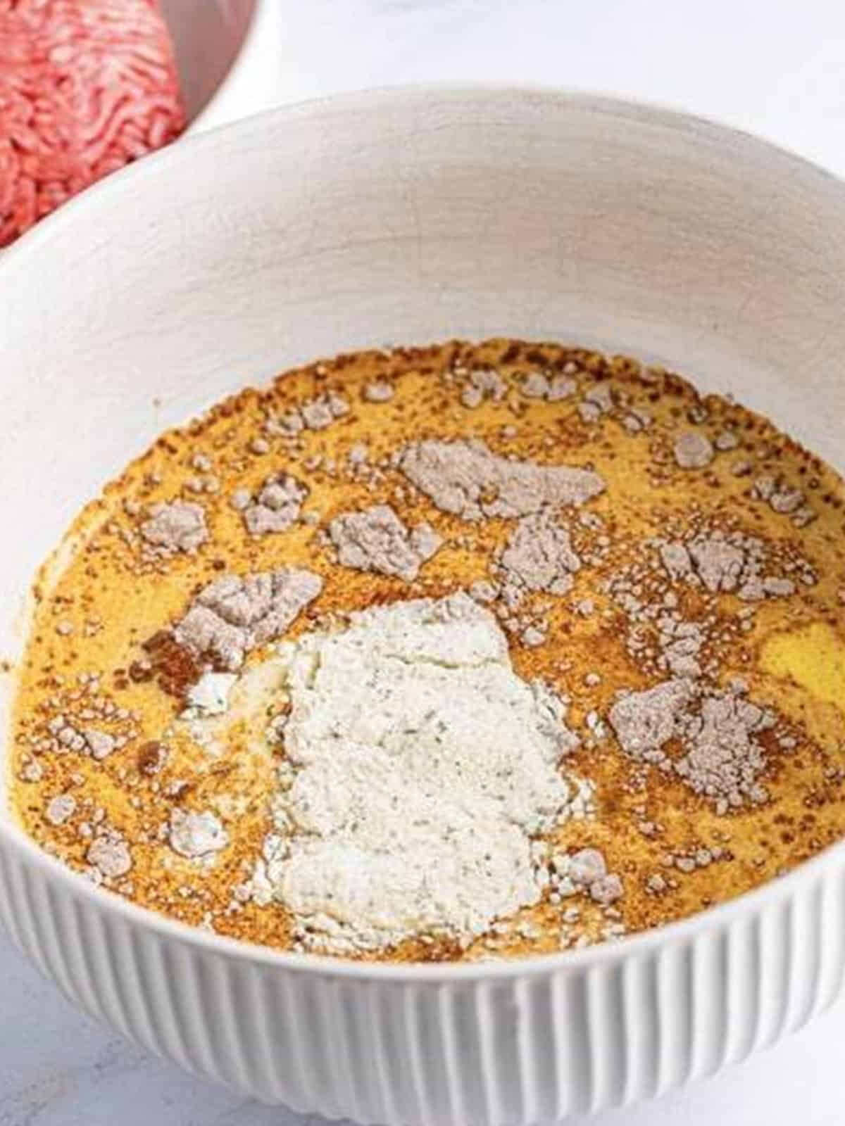 Milk, eggs, sugar, au jus mix, and ranch seasoning added to a large white bowl for crockpot meatloaf.