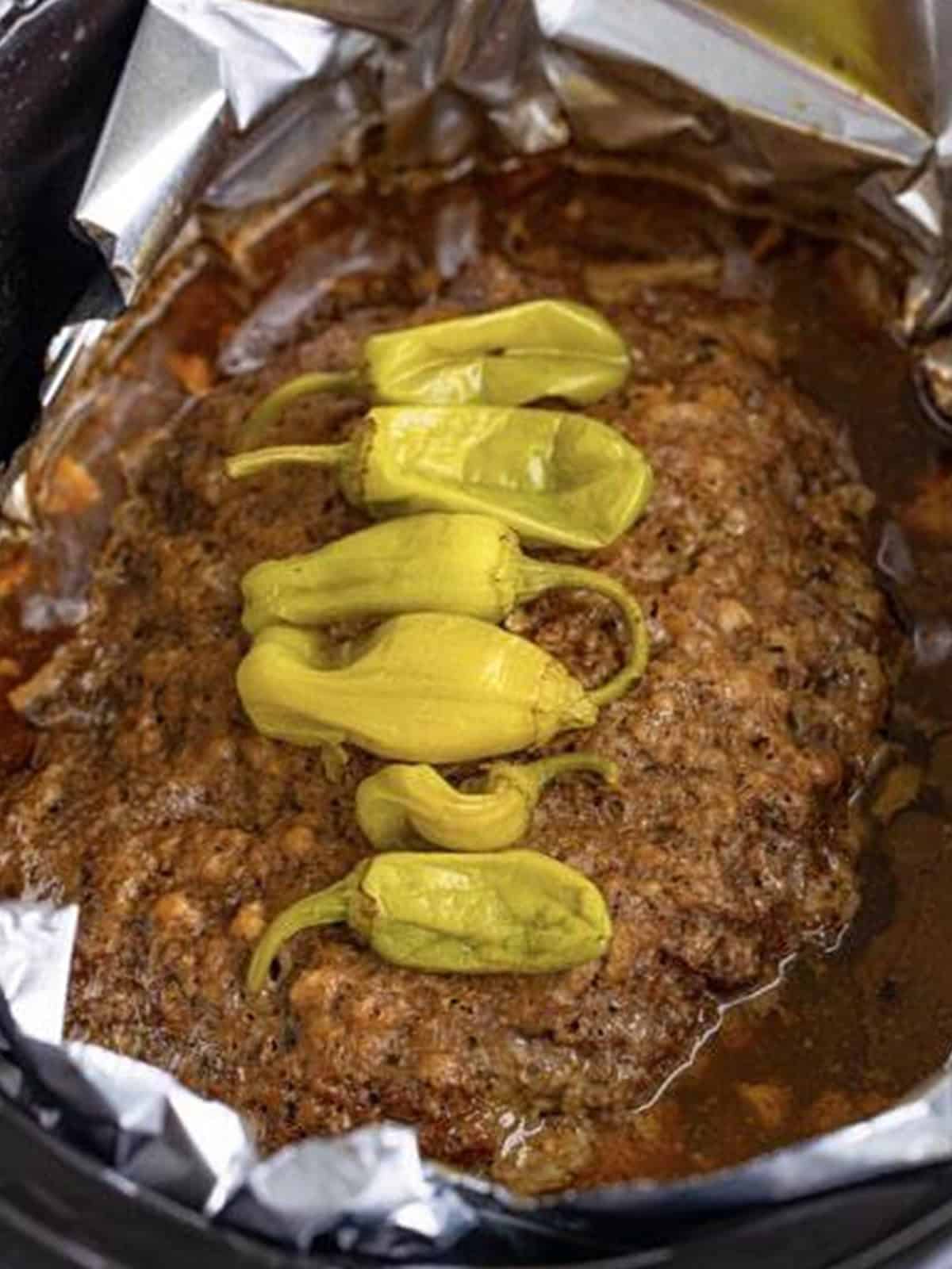 Crockpot meatloaf fully cooked in the slow cooker with gravy and pepperoncini.