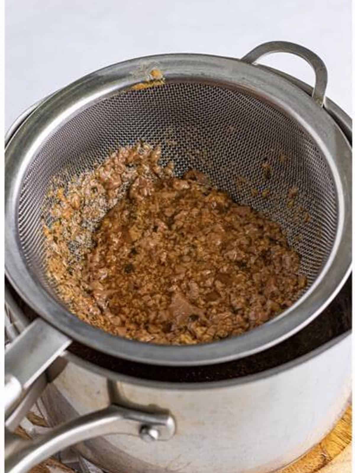 Slow cooker gravy strained through a sieve into a sauce pot.