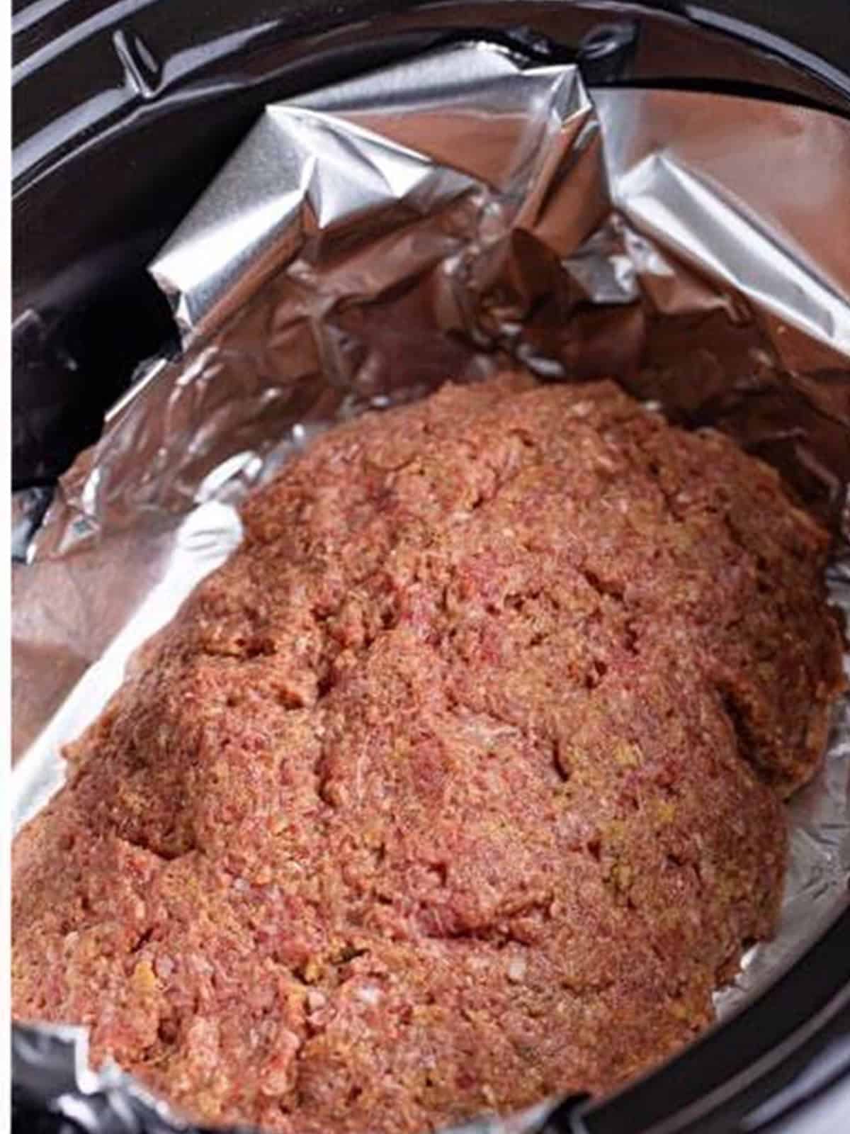 Meatloaf shaped into an oval on foil inside the slow cooker.