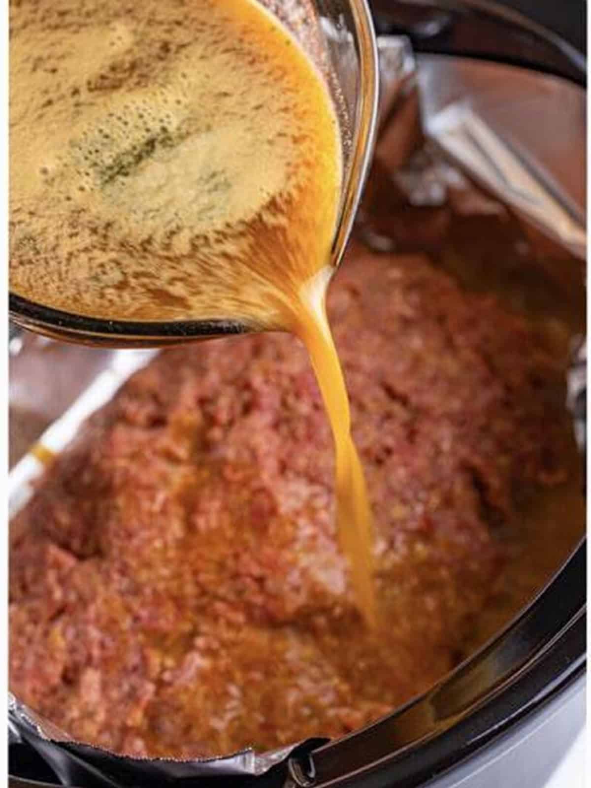 Gravy poured over the shaped meatloaf in the slow cooker.
