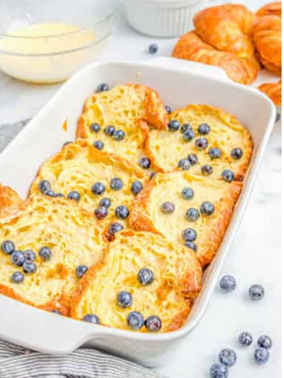 Croissant french toast topped with fresh blueberries in the baking dish before baking.