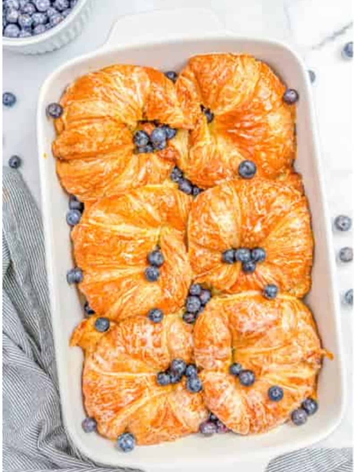 Golden baked blueberry croissant french toast in a white baking dish.