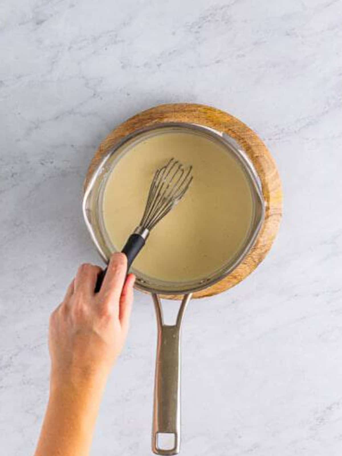 Whisking a smooth bechamel sauce in a saucepan for croque monsieur.