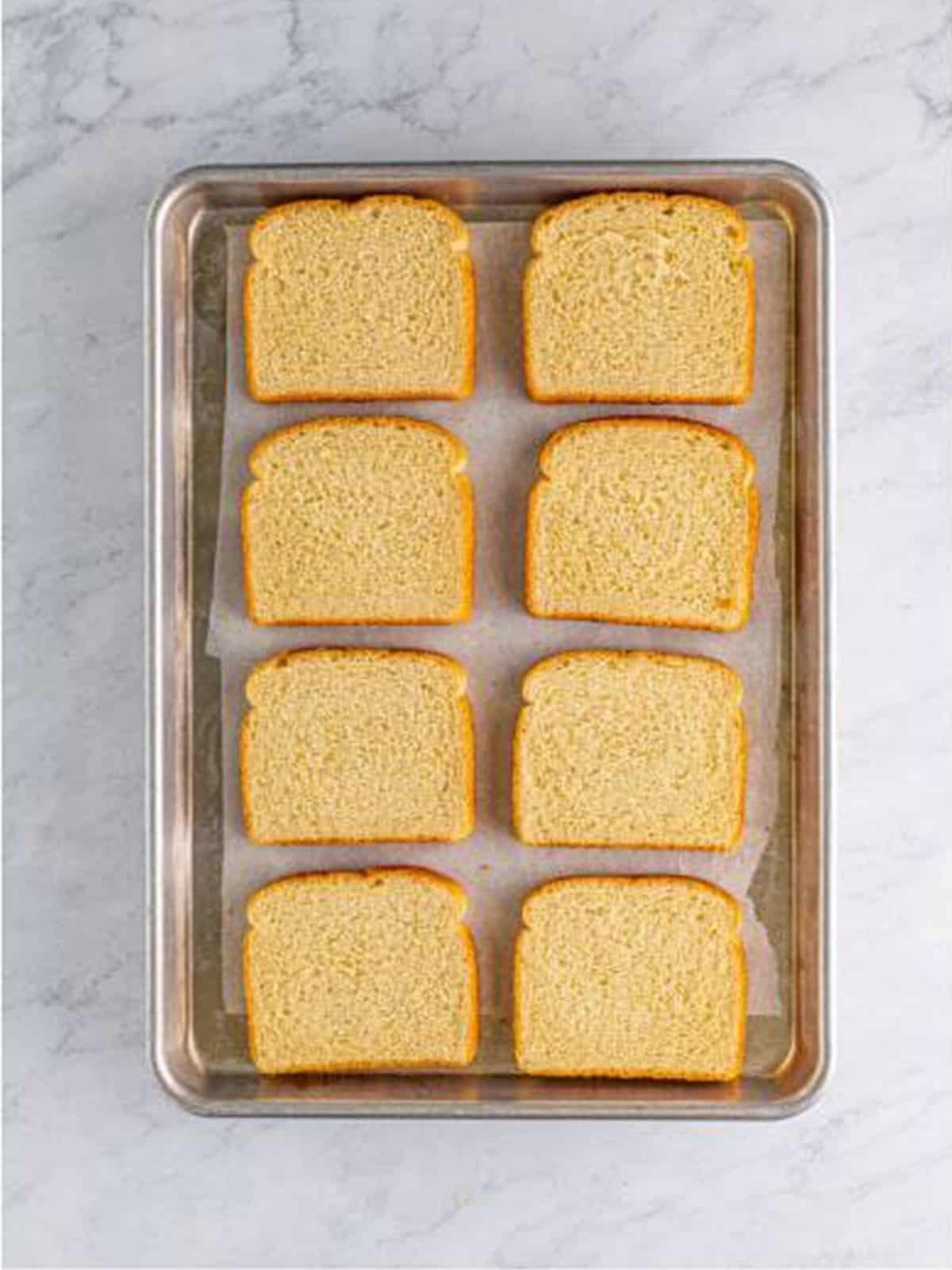 White bread slices toasting on a sheet tray for croque monsieur.