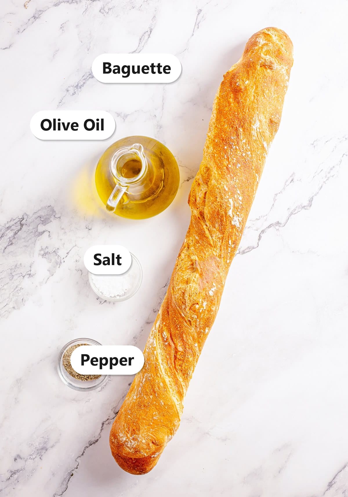 Labeled crostini ingredients including a French baguette, olive oil, salt, and pepper on a marble counter.