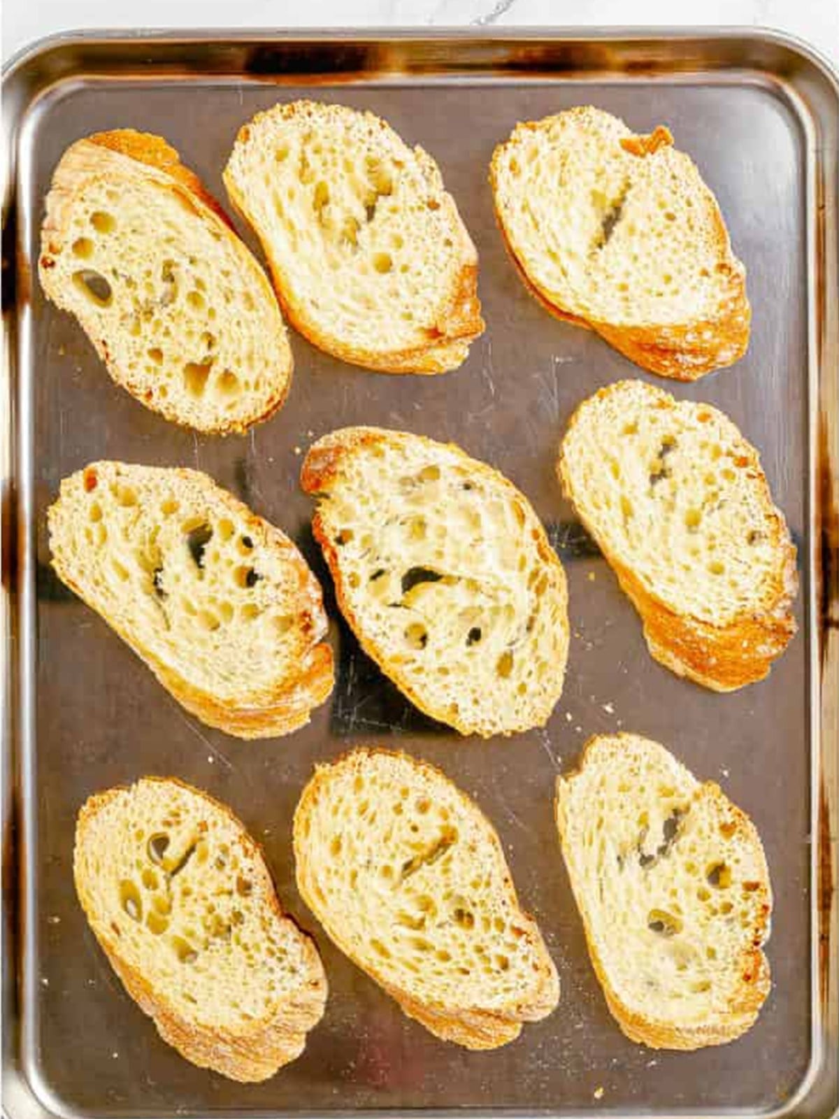 Sliced French baguette arranged on a parchment-lined baking sheet for crostini.