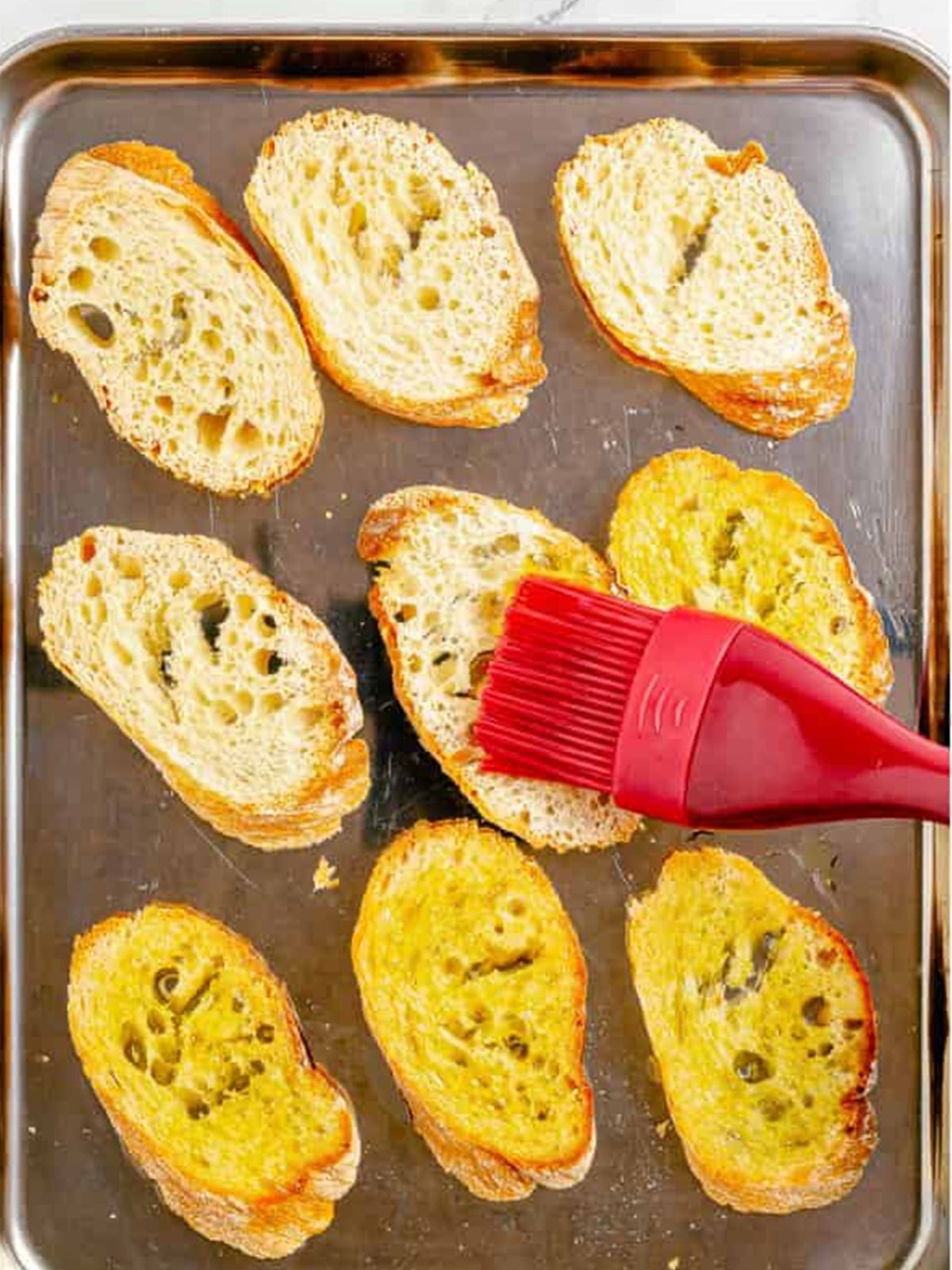 Brushing baguette slices with olive oil on a baking sheet for crostini.