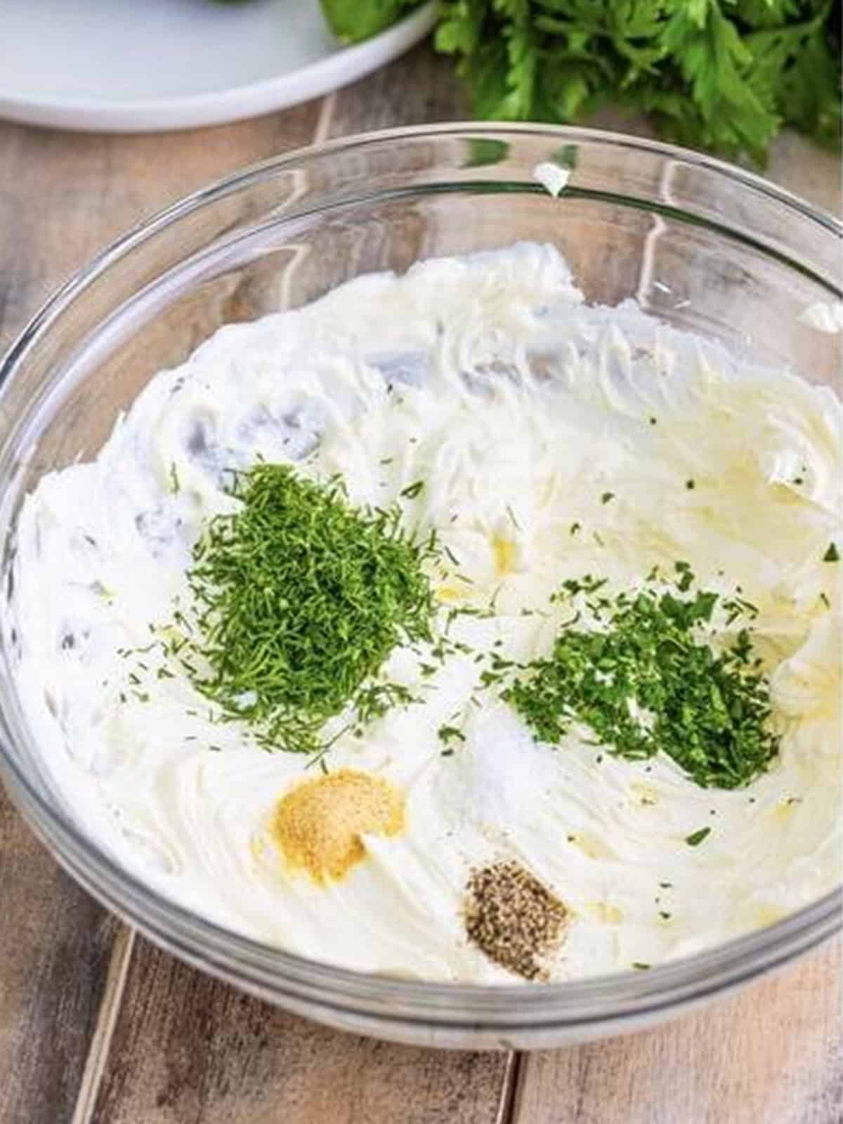 Whipped cream cheese topped with fresh dill, parsley, garlic powder, salt, and pepper in a bowl.