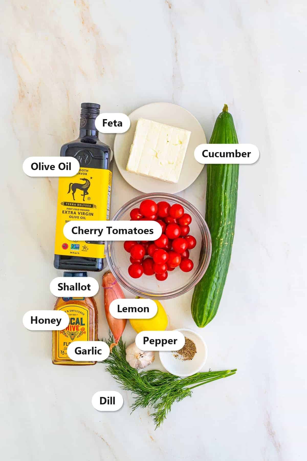 Ingredients for cucumber tomato feta salad including cucumber, cherry tomatoes, feta, olive oil, lemon, dill, shallot, garlic, and honey.