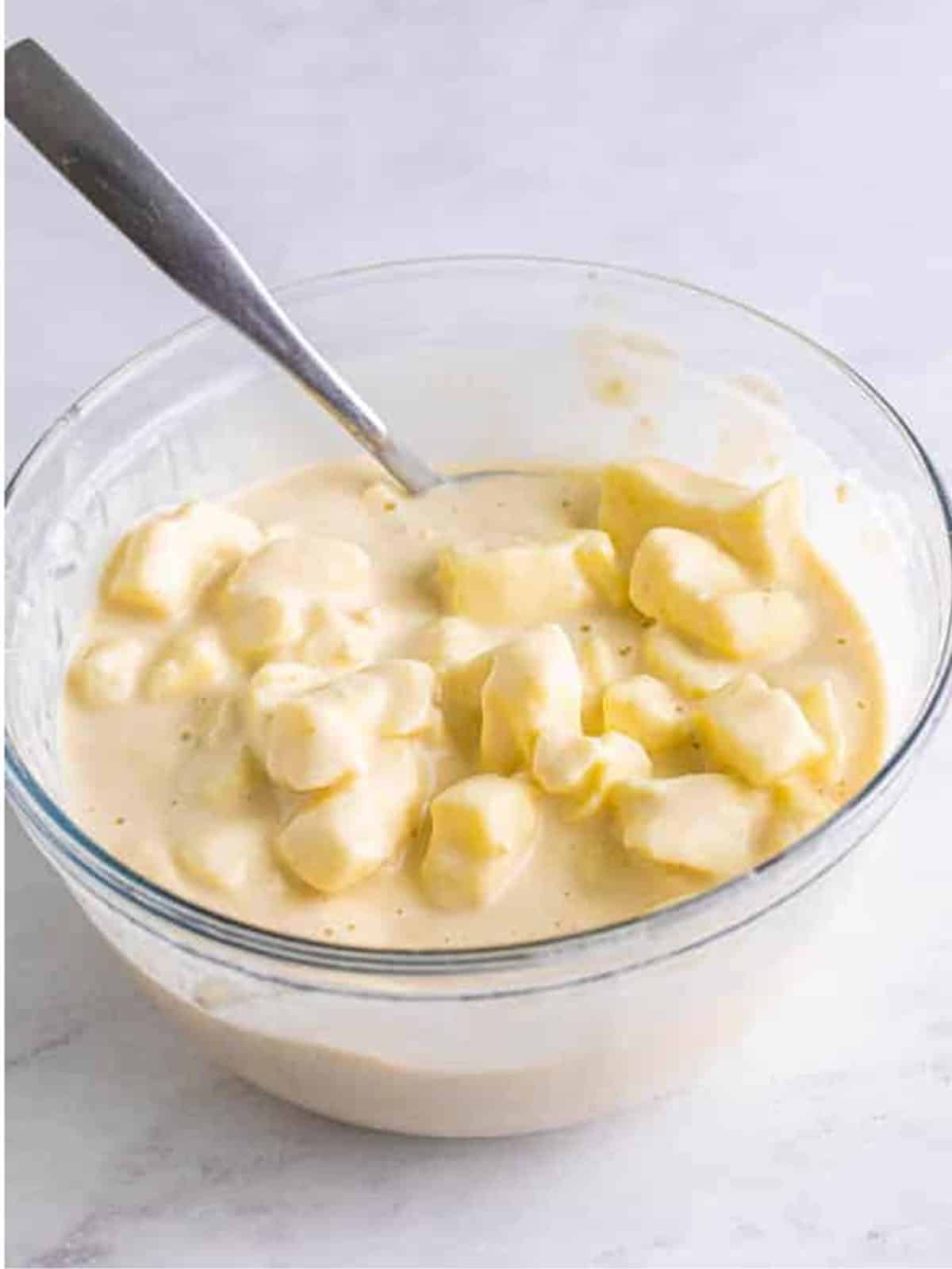 Cold cheese curds coated in the batter in a glass bowl.