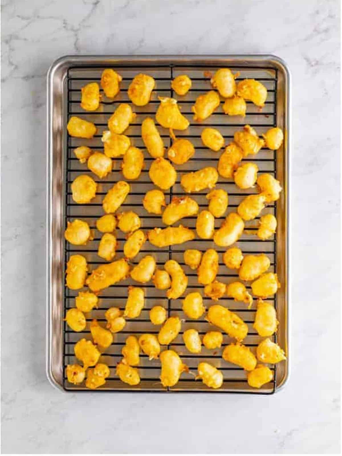 Golden fried cheese curds draining on a wire rack over a sheet tray.