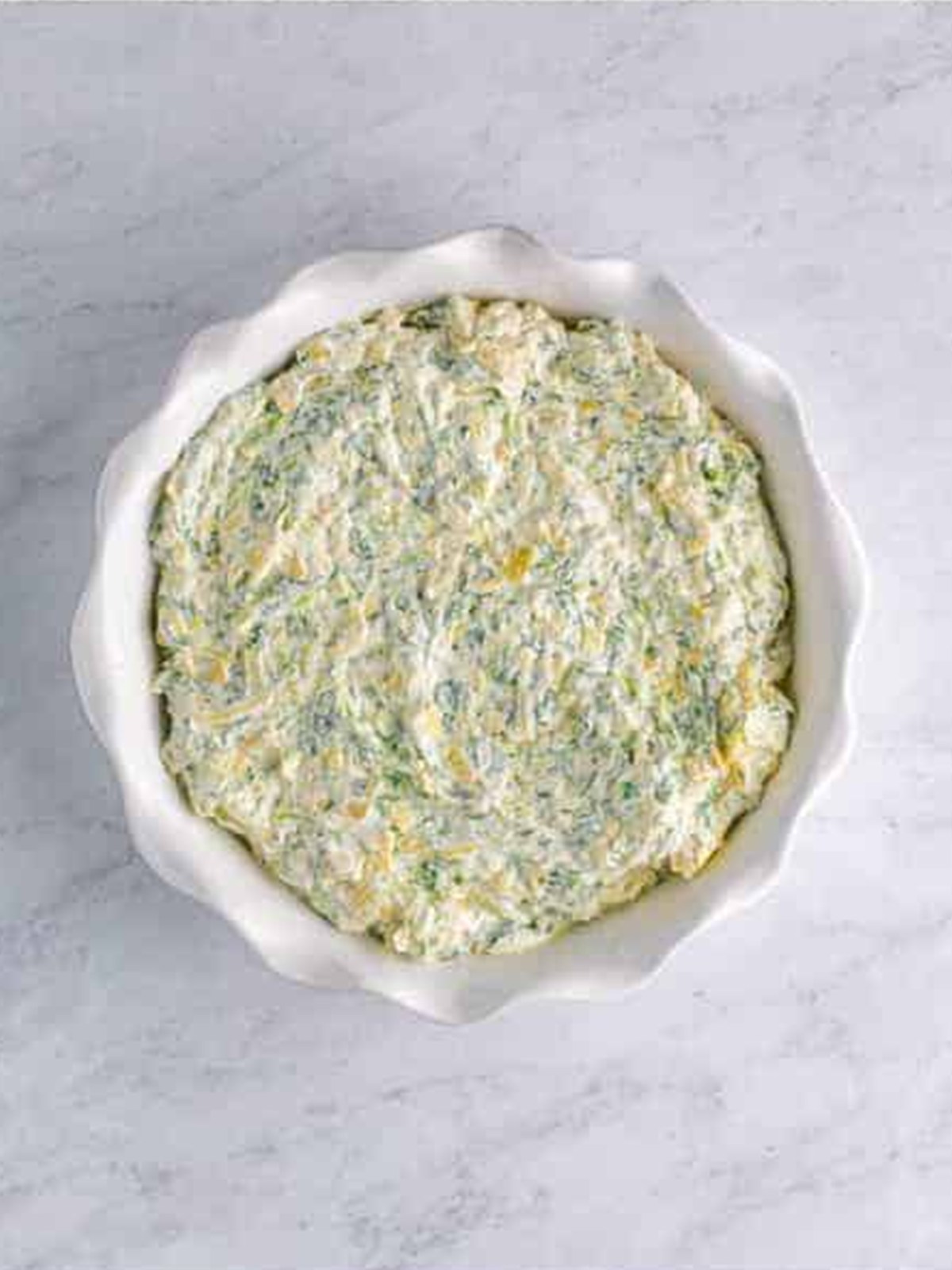 Spinach artichoke dip spread into a white baking dish.
