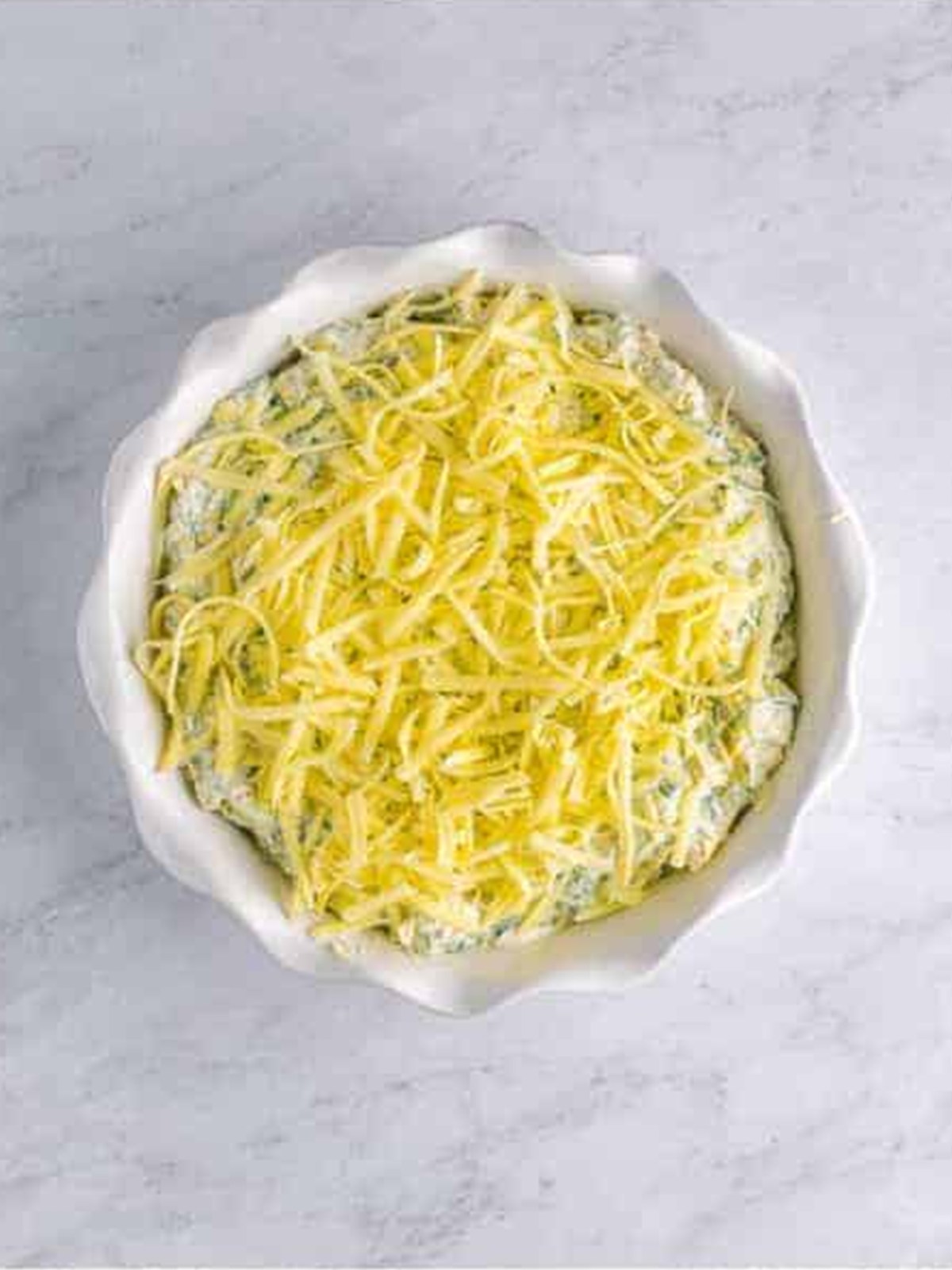 Spinach artichoke dip topped with shredded mozzarella before baking.