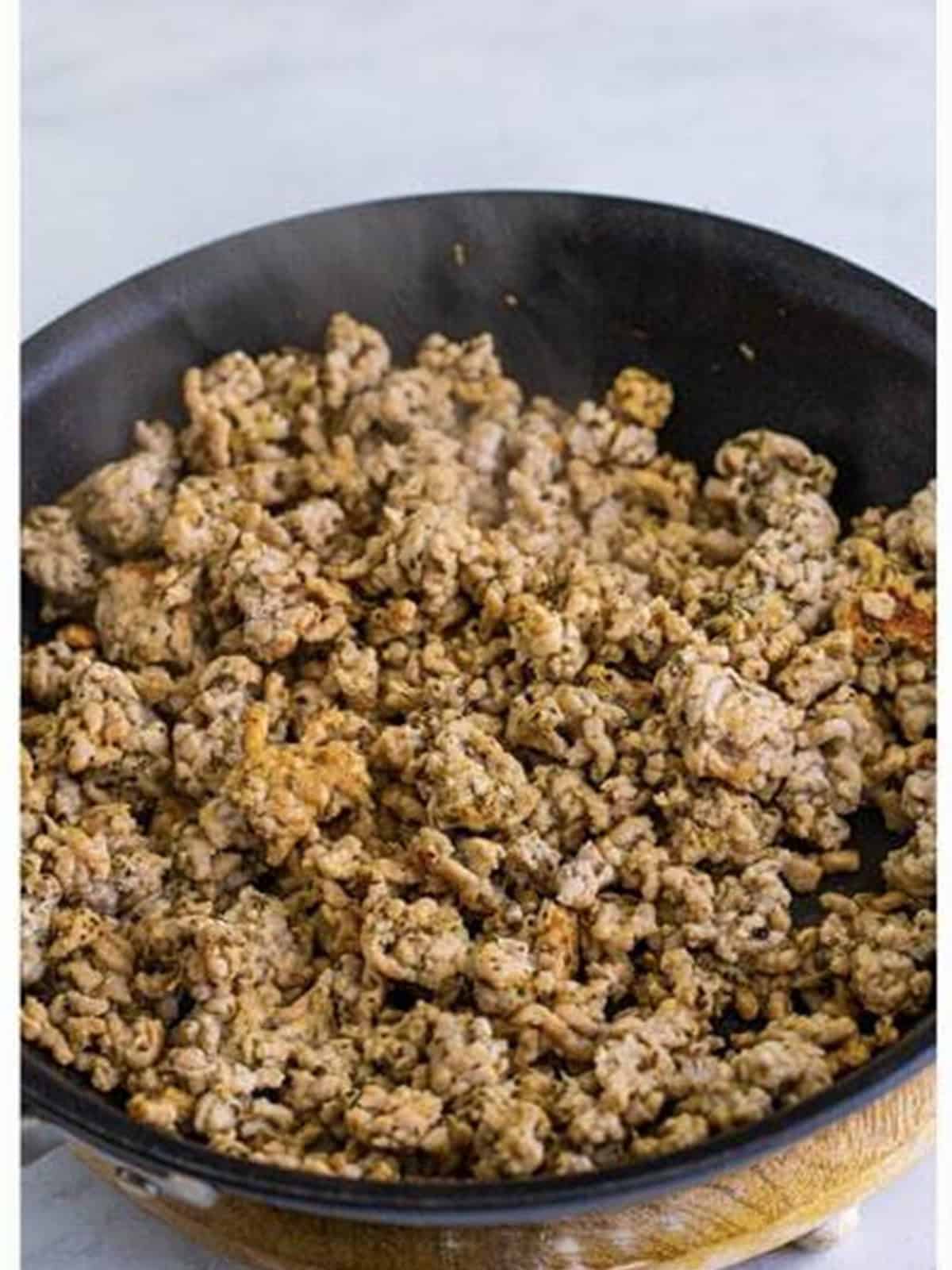 Cooking crumbled Italian sausage in a skillet for deep dish pizza.