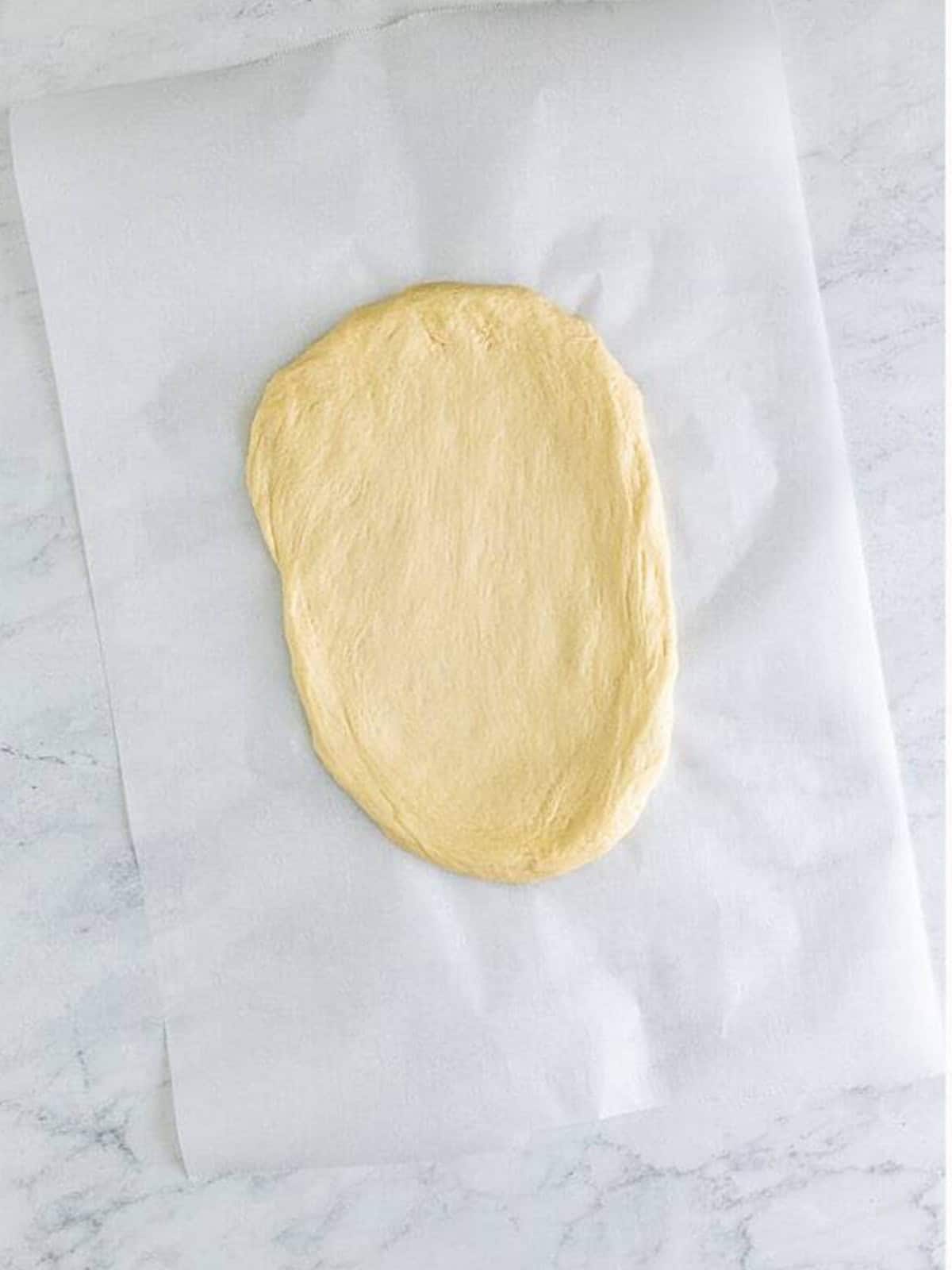 Pizza dough stretched on parchment paper for deep dish pizza.