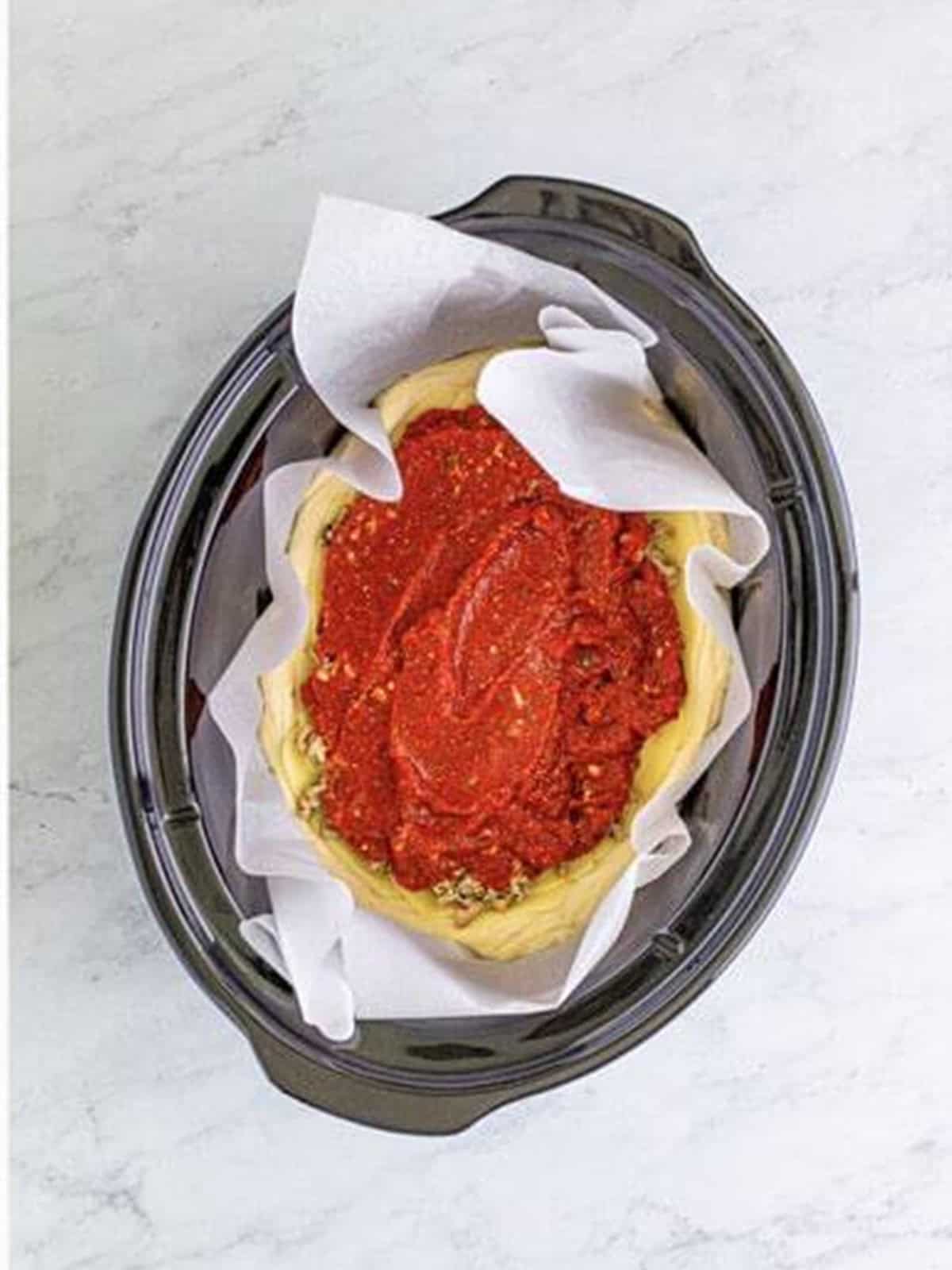 Spreading pizza sauce over the deep dish pizza in the slow cooker.
