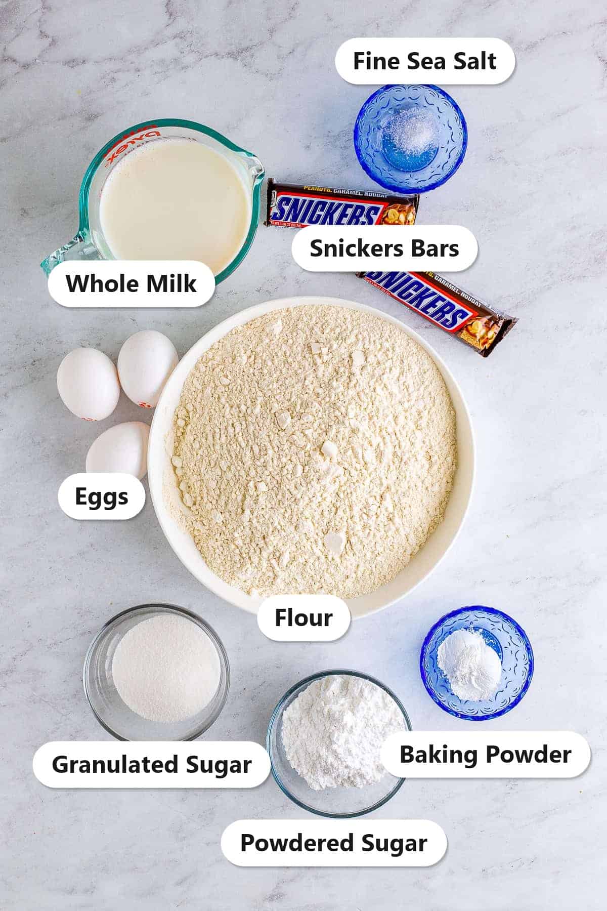 Labeled ingredients for deep fried snickers including Snickers bars, whole milk, eggs, flour, granulated sugar, powdered sugar, baking powder, and fine sea salt.