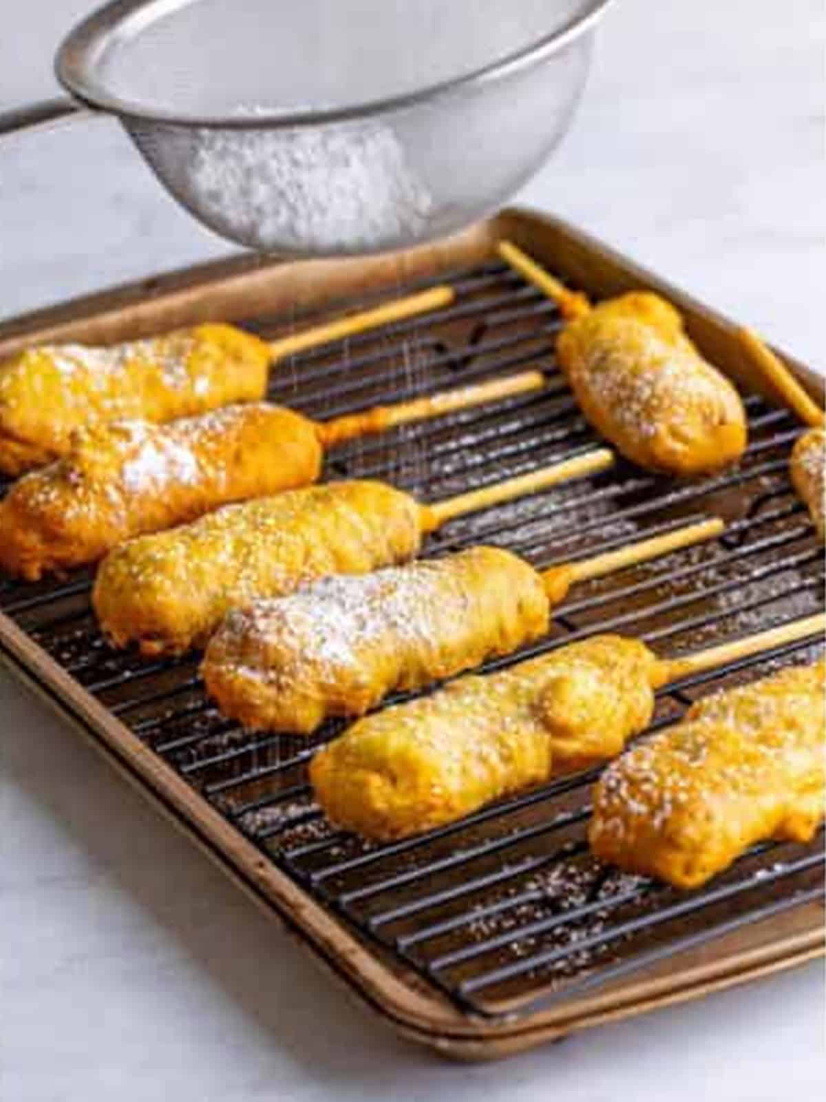 Deep fried Snickers bars resting on a wire rack dusted with powdered sugar.