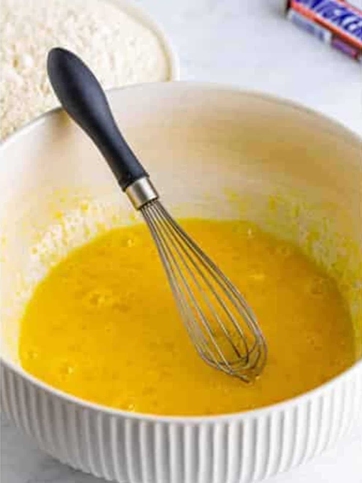 Eggs and sugar whisked smooth with milk in a large white bowl for the batter.