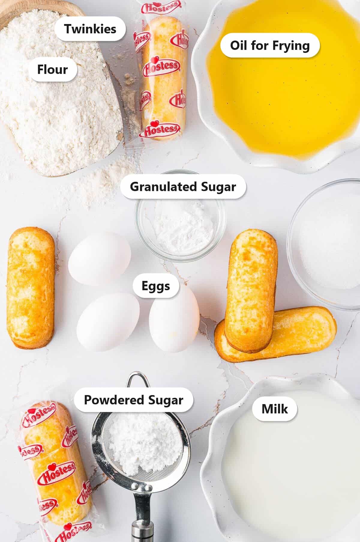 Labeled ingredients for deep fried Twinkies including Twinkies, flour, eggs, milk, sugar, and oil for frying.
