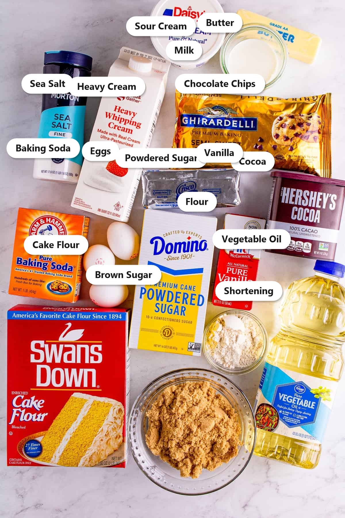 Labeled ingredients for ding dong cake including chocolate chips, cocoa, cake flour, sour cream, brown sugar, butter, shortening, and powdered sugar.