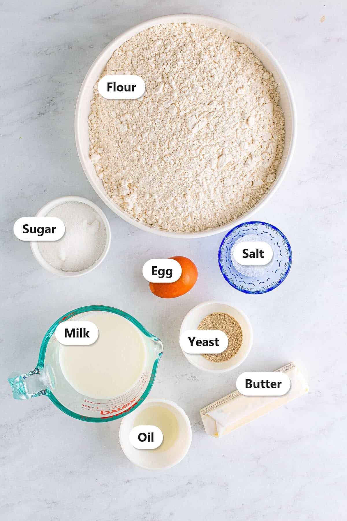 Labeled ingredients to make dinner rolls including flour, sugar, egg, salt, milk, yeast, butter, and oil.