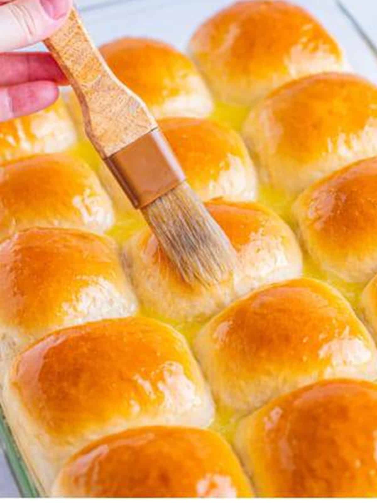 Golden baked dinner rolls being brushed with melted butter.