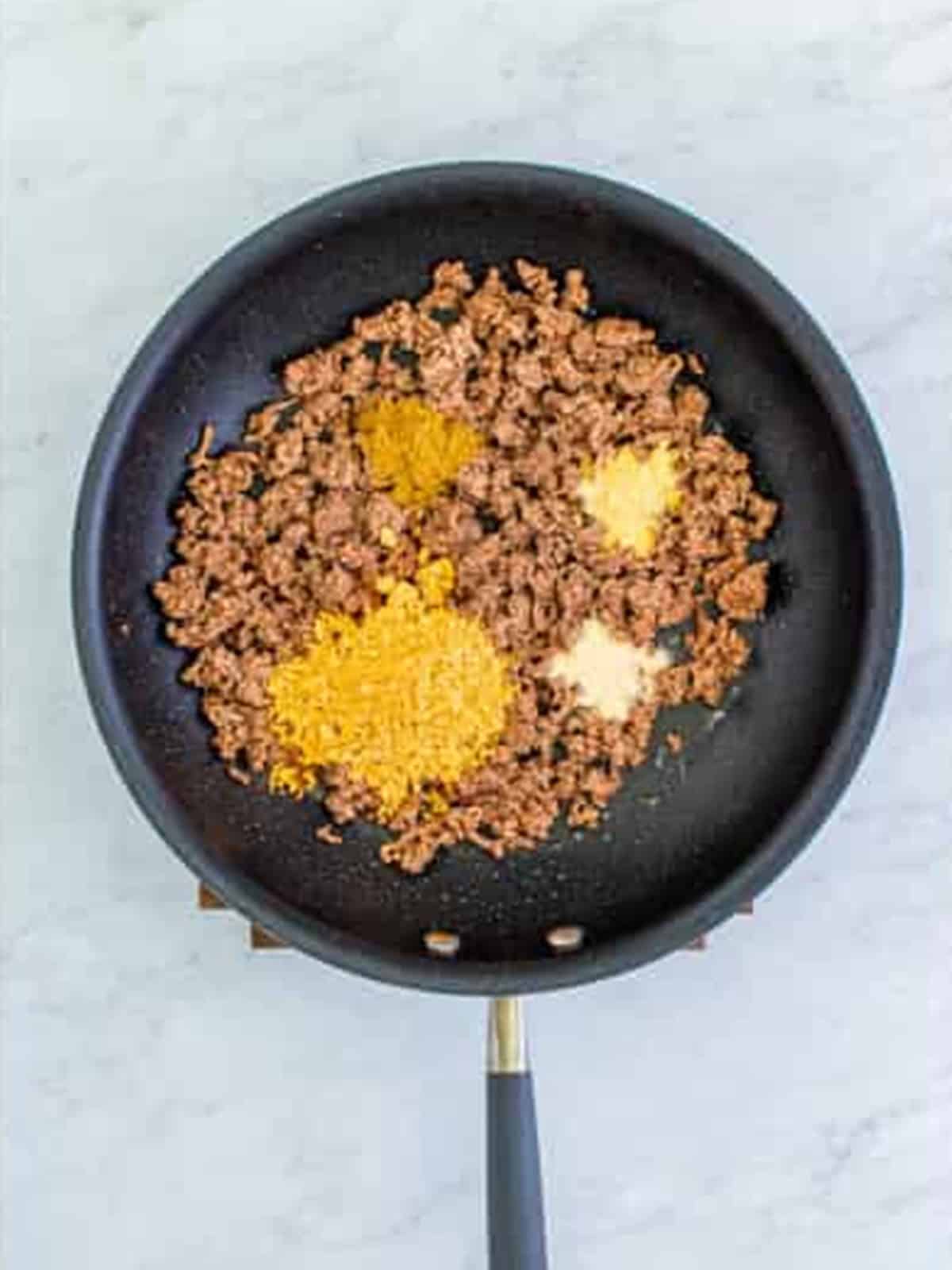 Adding taco seasoning, cumin, garlic, and onion powder to the beef for Doritos Taco Salad.