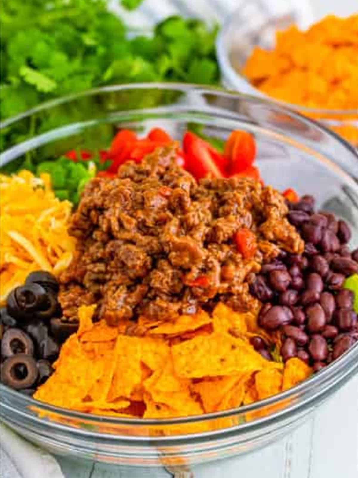 Combining romaine, Doritos, cheese, beans, tomatoes, and beef in a bowl for Doritos Taco Salad.