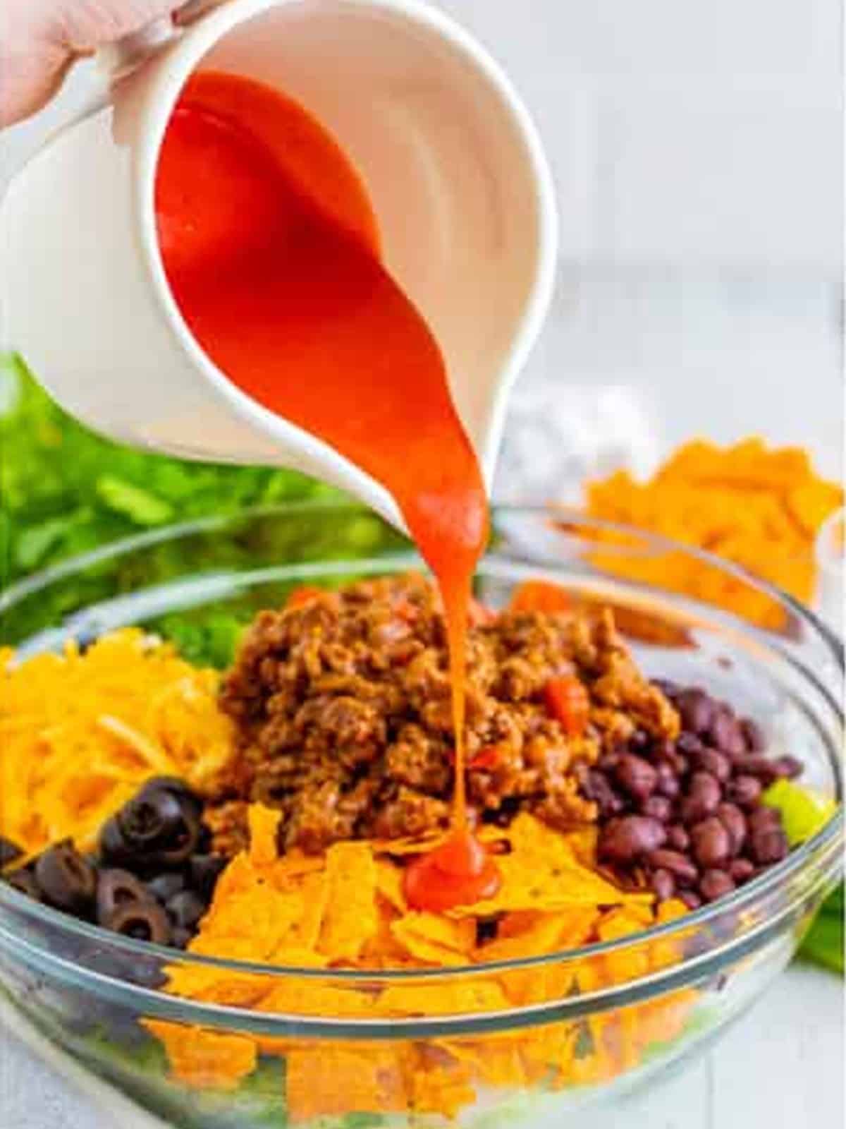 Pouring Catalina dressing over the Doritos Taco Salad before tossing.