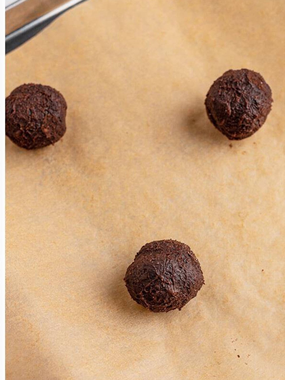 Scooped double chocolate chip cookie dough balls on a parchment lined sheet tray ready to bake.