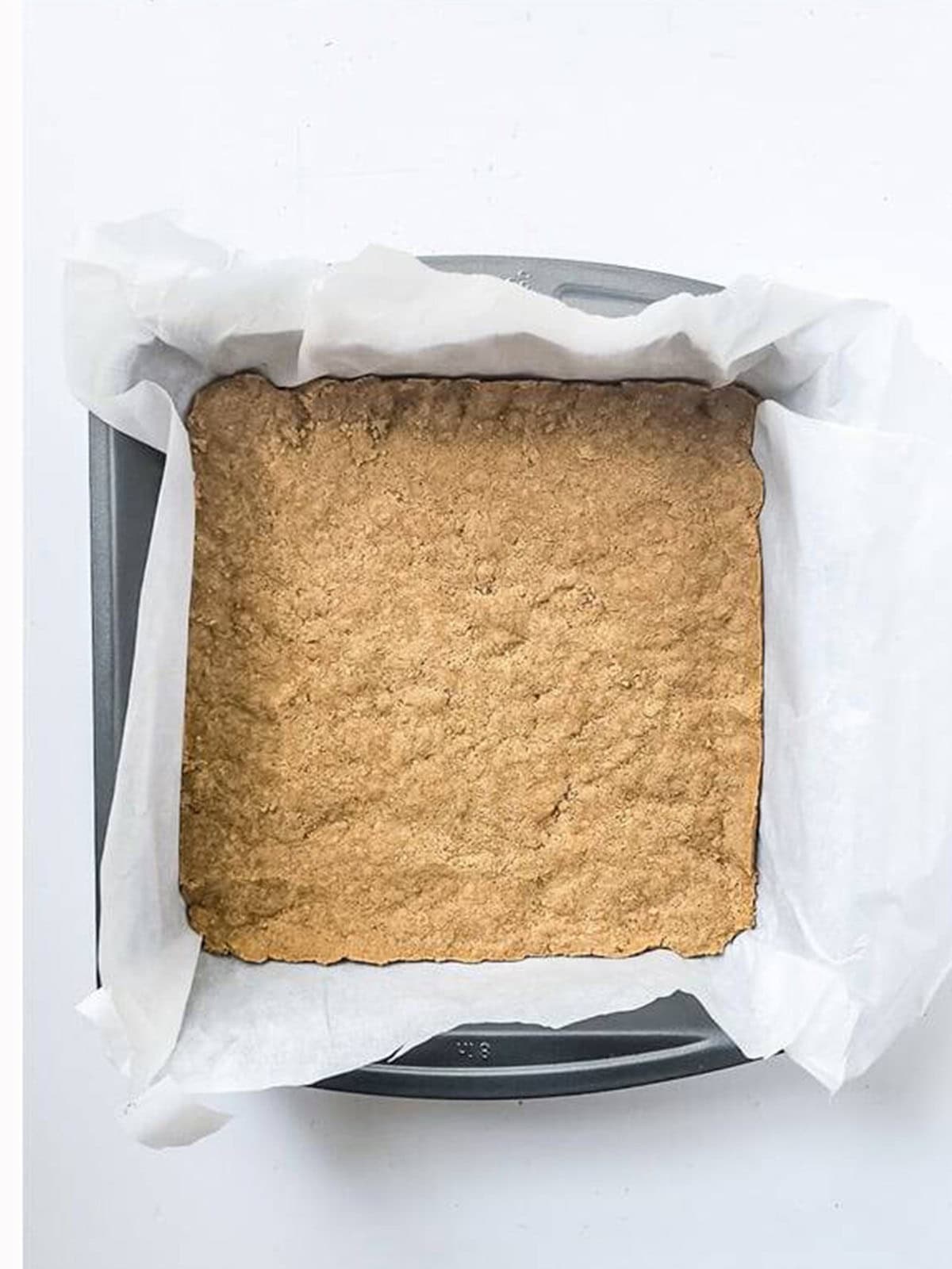 Graham cracker crust pressed into a parchment-lined square baking pan.