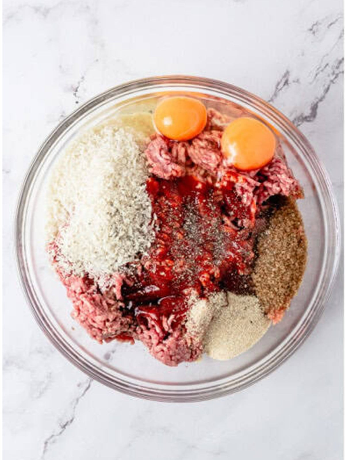 Panko, ketchup, eggs, brown sugar, and seasonings added to ground beef in a glass bowl.