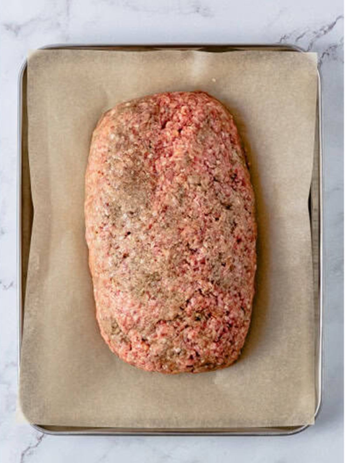 Raw meatloaf mixture shaped into a loaf on a parchment lined sheet pan.
