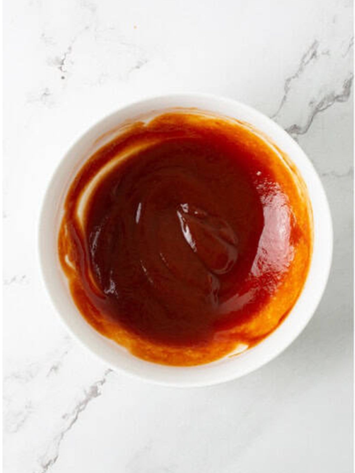 Ketchup and brown sugar glaze whisked together in a white bowl.