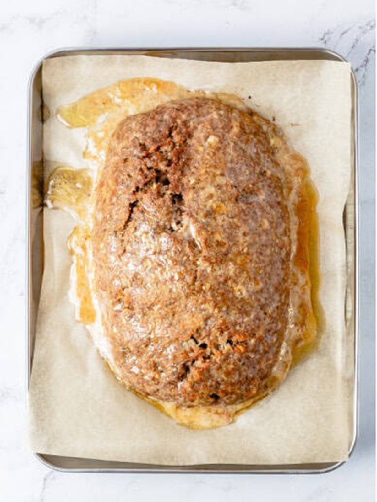 Baked meatloaf on a parchment lined sheet pan before glazing.