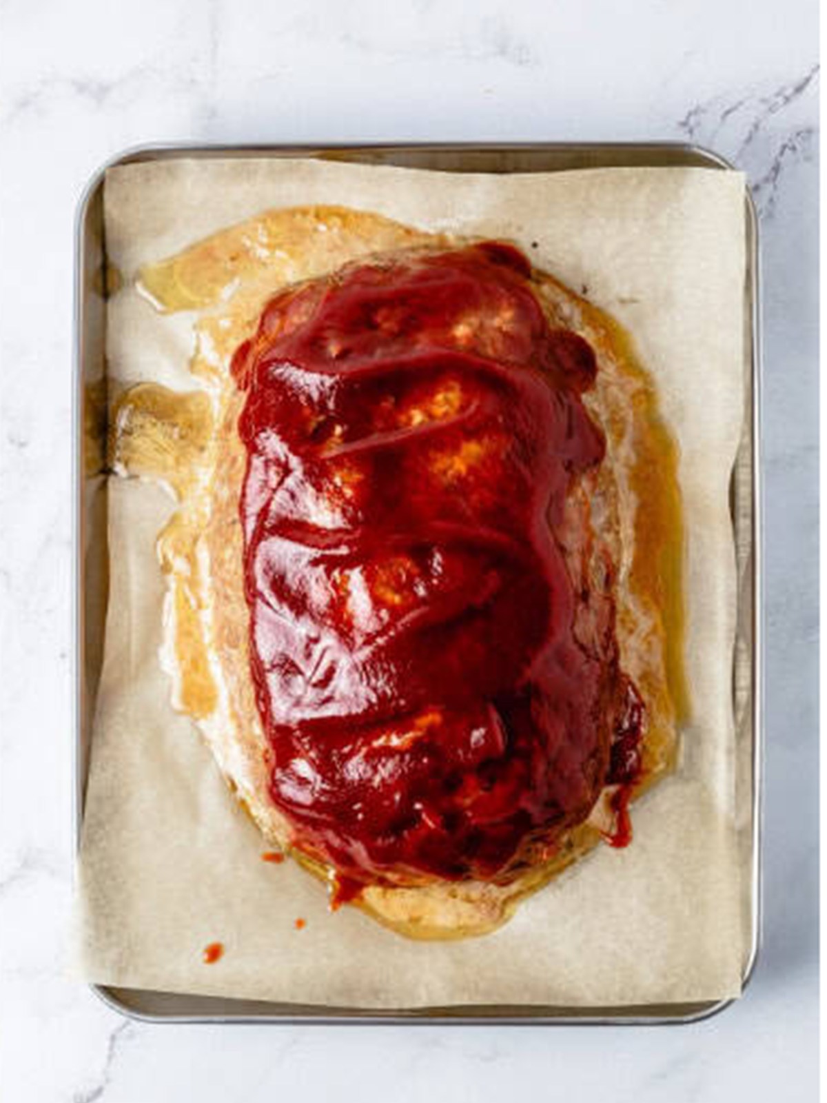 Glazed meatloaf brushed with ketchup glaze on a sheet pan after baking.