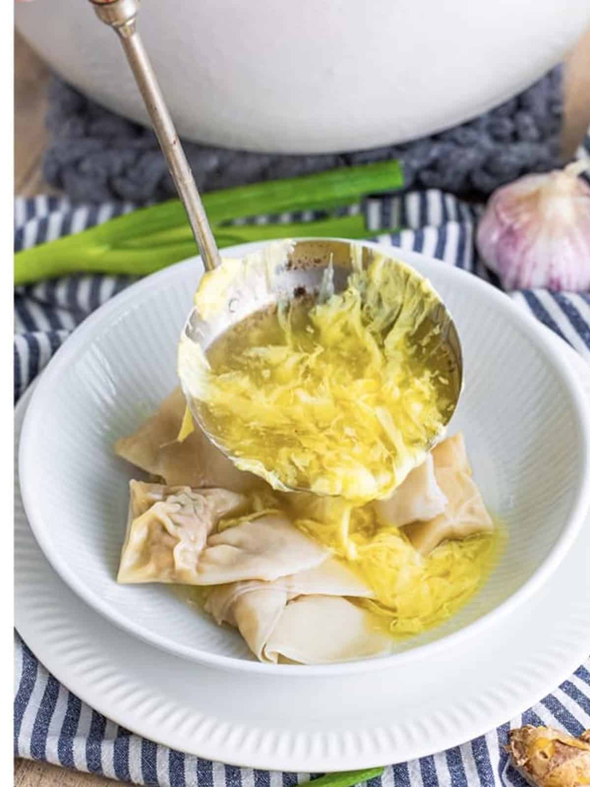Hot egg drop soup ladled over wontons in a white bowl.