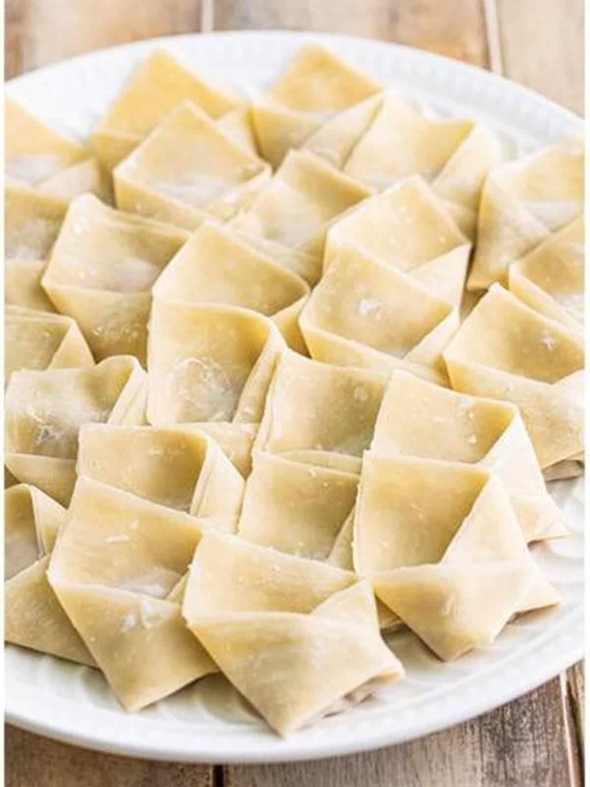 A plate of folded raw wontons for egg drop soup.