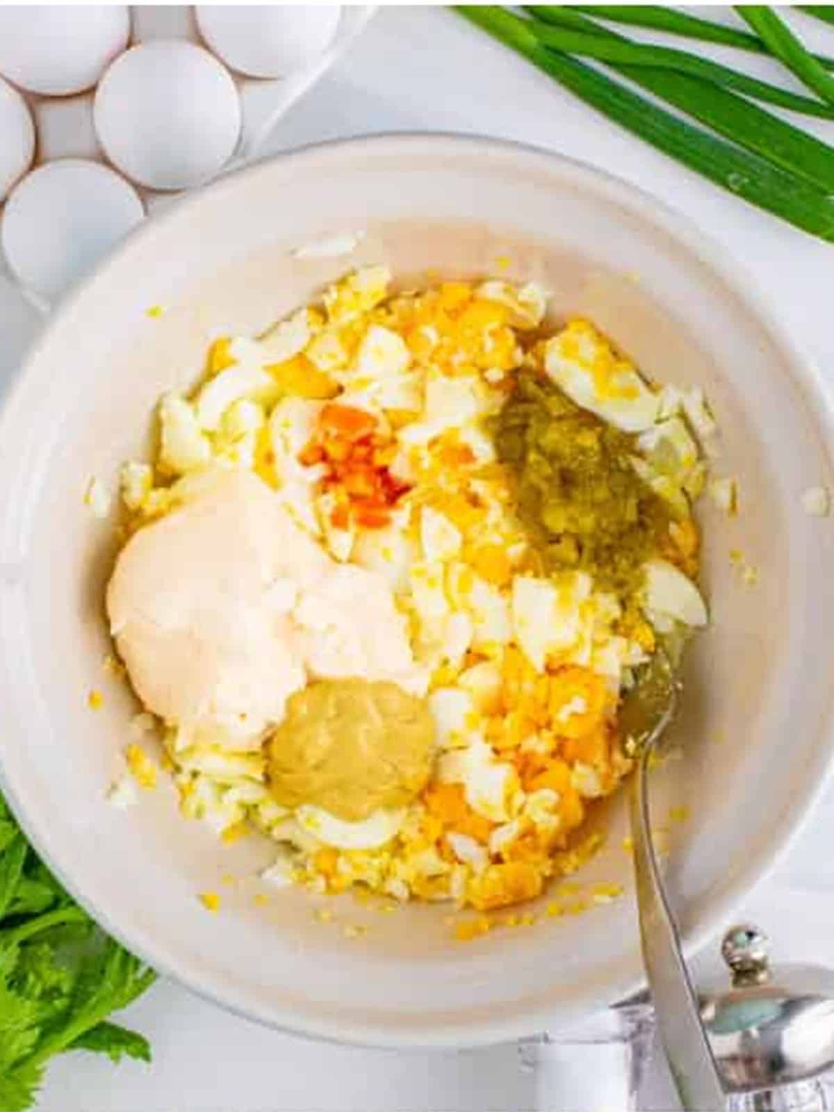 Chopped hard-boiled eggs with mayonnaise, dijon, relish, and hot sauce in a bowl for egg salad sandwich.