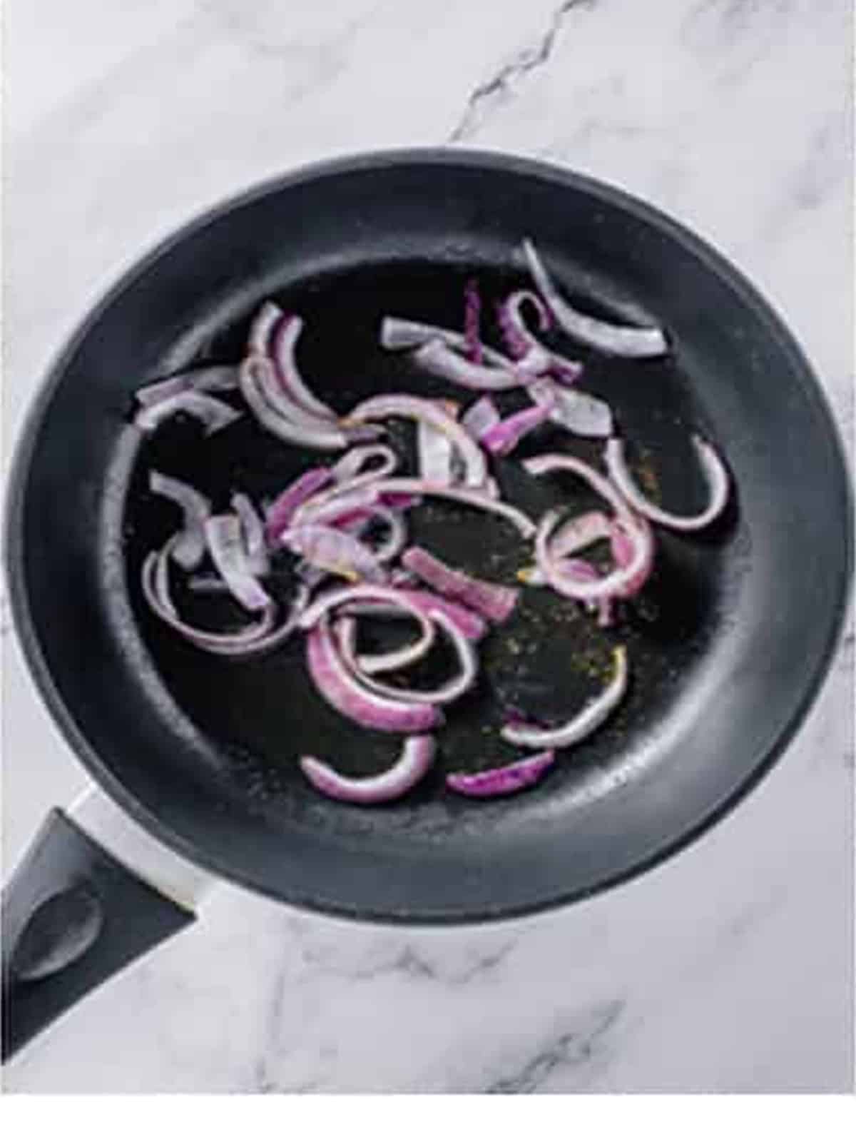 Sliced red onion sauteing in olive oil in a black skillet.