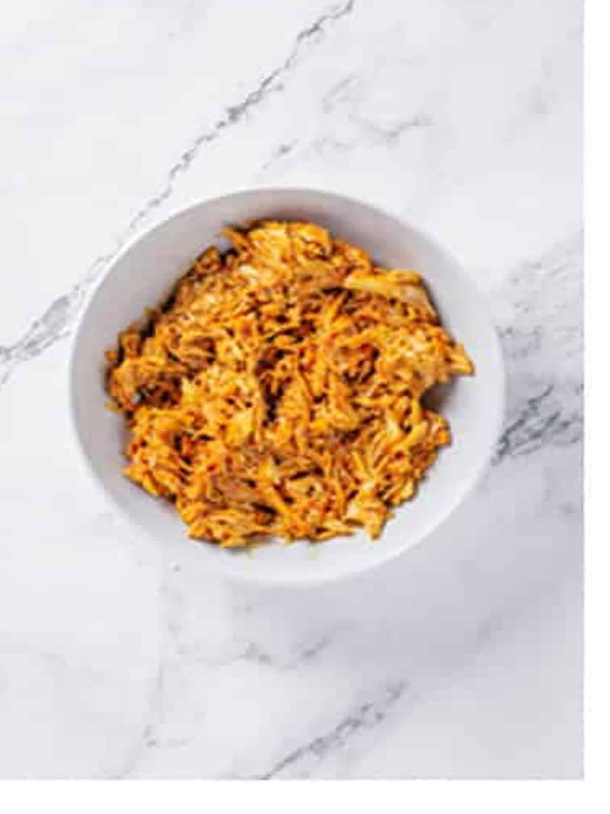 Shredded cooked chicken tossed in BBQ sauce in a white bowl.