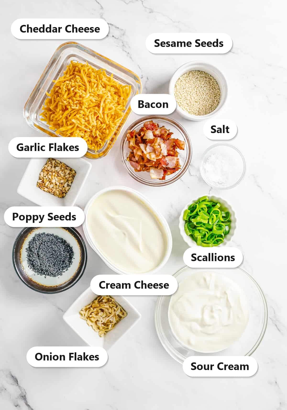 Labeled ingredients for everything bagel cheese ball including cream cheese, cheddar, sour cream, bacon, scallions, and everything bagel seasonings.
