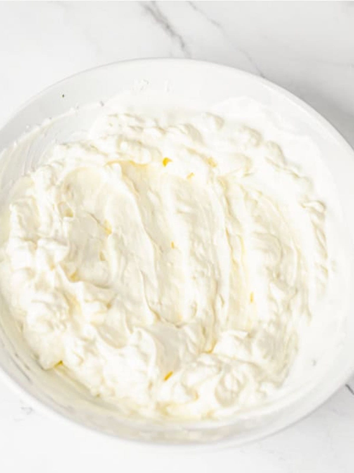 Cream cheese and sour cream whipped smooth in a white bowl.