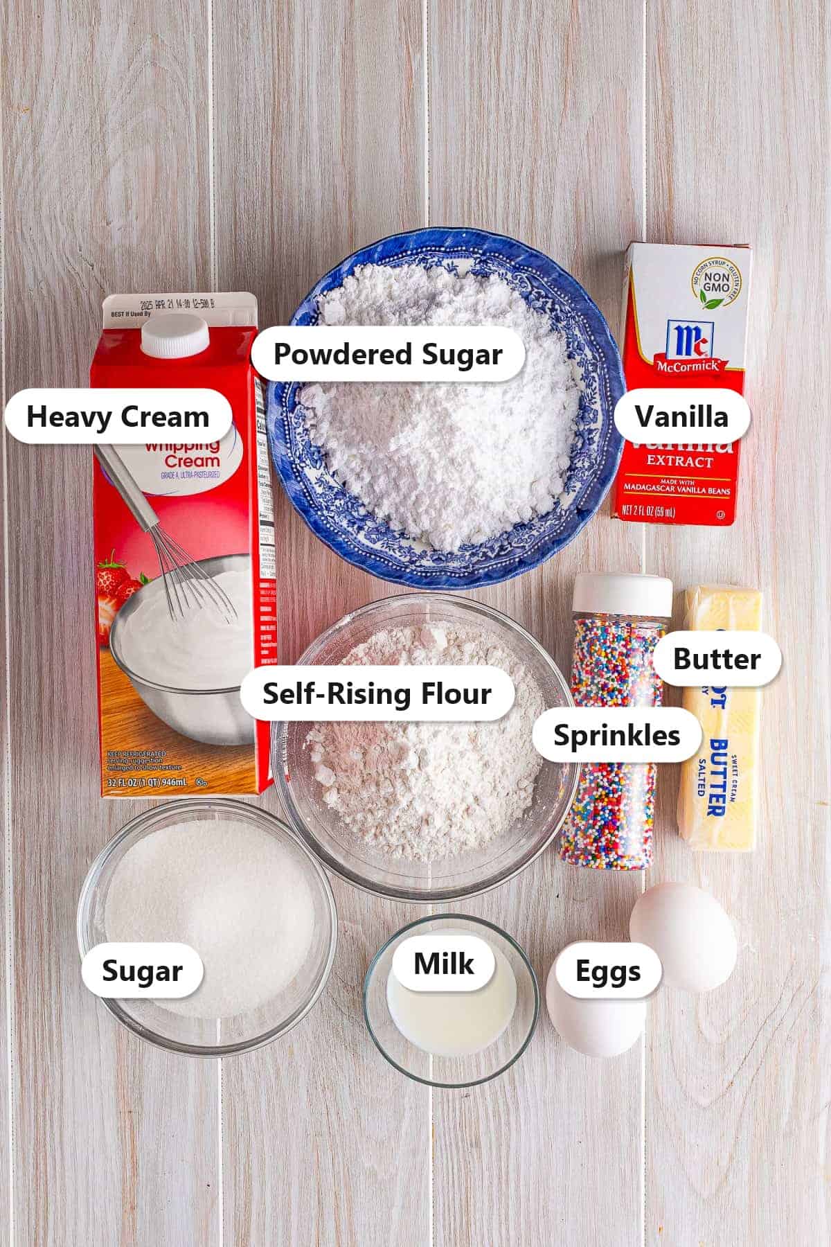Labeled ingredients for fairy cakes including butter, sugar, eggs, self-rising flour, vanilla, milk, sprinkles, and glaze ingredients.