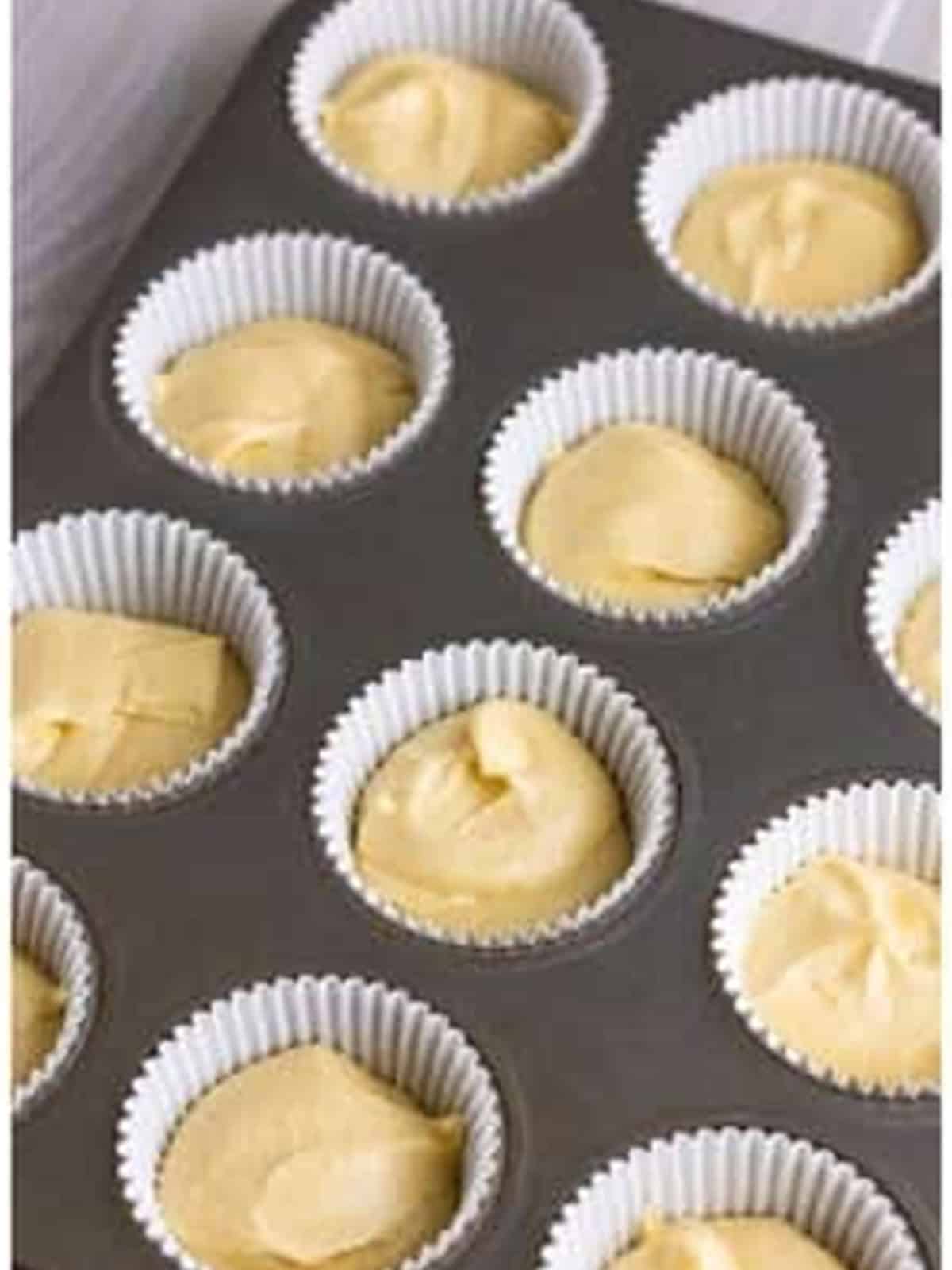 Fairy cake batter divided into paper liners in a muffin tin.